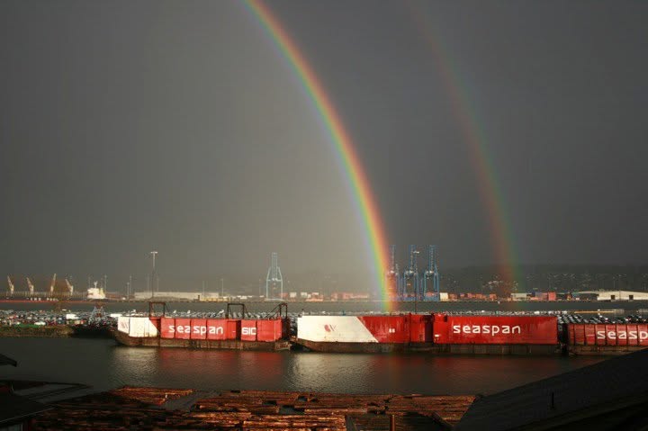 A double rainbow arcing over the harbour and moored barges.